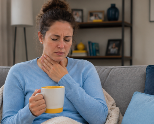 Woman with a sore throat holding a warm drink while resting at home