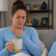 Woman with a sore throat holding a warm drink while resting at home