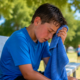 Young athlete sitting on a bench outdoors while cooling off with a towel after experiencing heat exhaustion symptoms.
