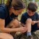 Adult examining a young child's leg outdoors after discovering a tick bite during a hike.