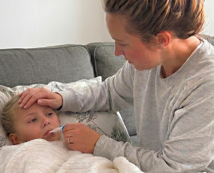 Parent checking a child's temperature with a thermometer while caring for them at home during an illness.