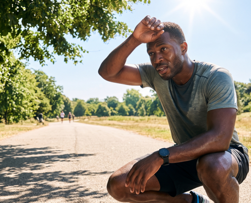 Man resting after exercising in summer heat while wiping sweat from his forehead outdoors