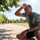 Man resting after exercising in summer heat while wiping sweat from his forehead outdoors