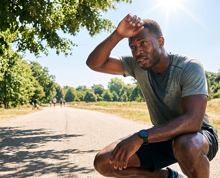 Man resting after exercising in summer heat while wiping sweat from his forehead outdoors
