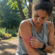 Woman examining a large red, swollen mosquito bite on her upper arm while outdoors.